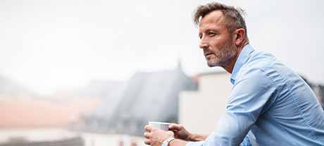 Man leaning on roof top balcony with cup of coffee