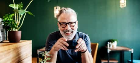 man sat at table smiling with coffee in hands
