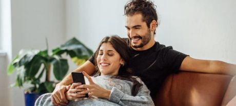Couple sat on sofa smiling at a phone