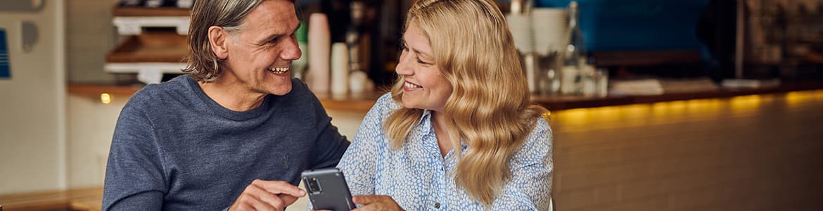 Man and woman smiling while sat down in a cafe looking at a phone