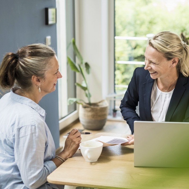 Two women talking at a table with a laptop