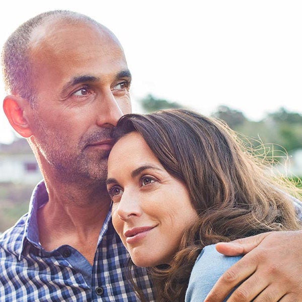 a couple outdoors hugging, looking in the distance