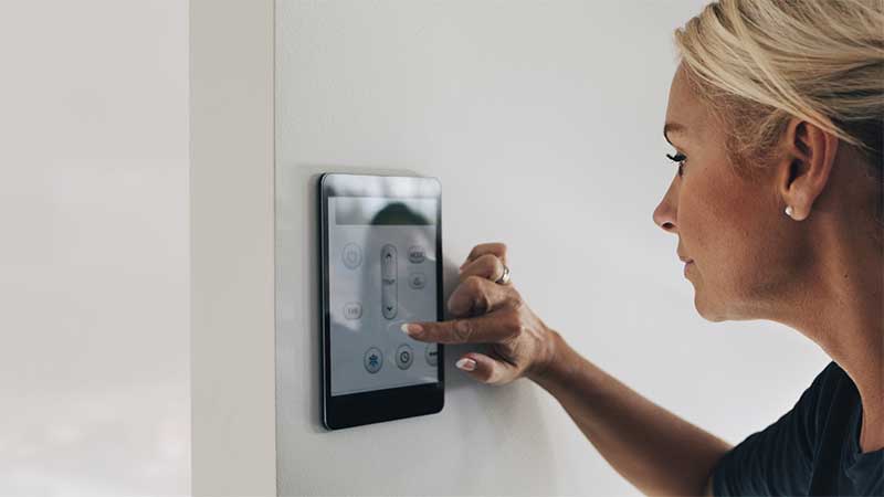 Woman using a thermostat app on a wall-mounted touch screen