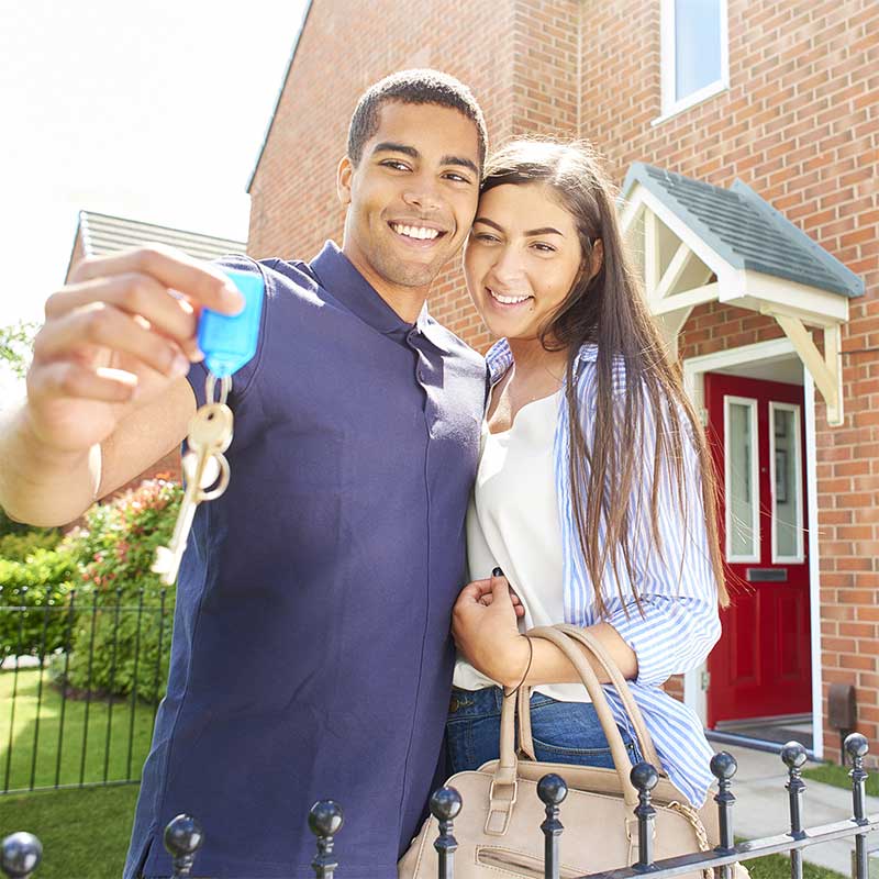 Man and woman holding keys in front of their new home