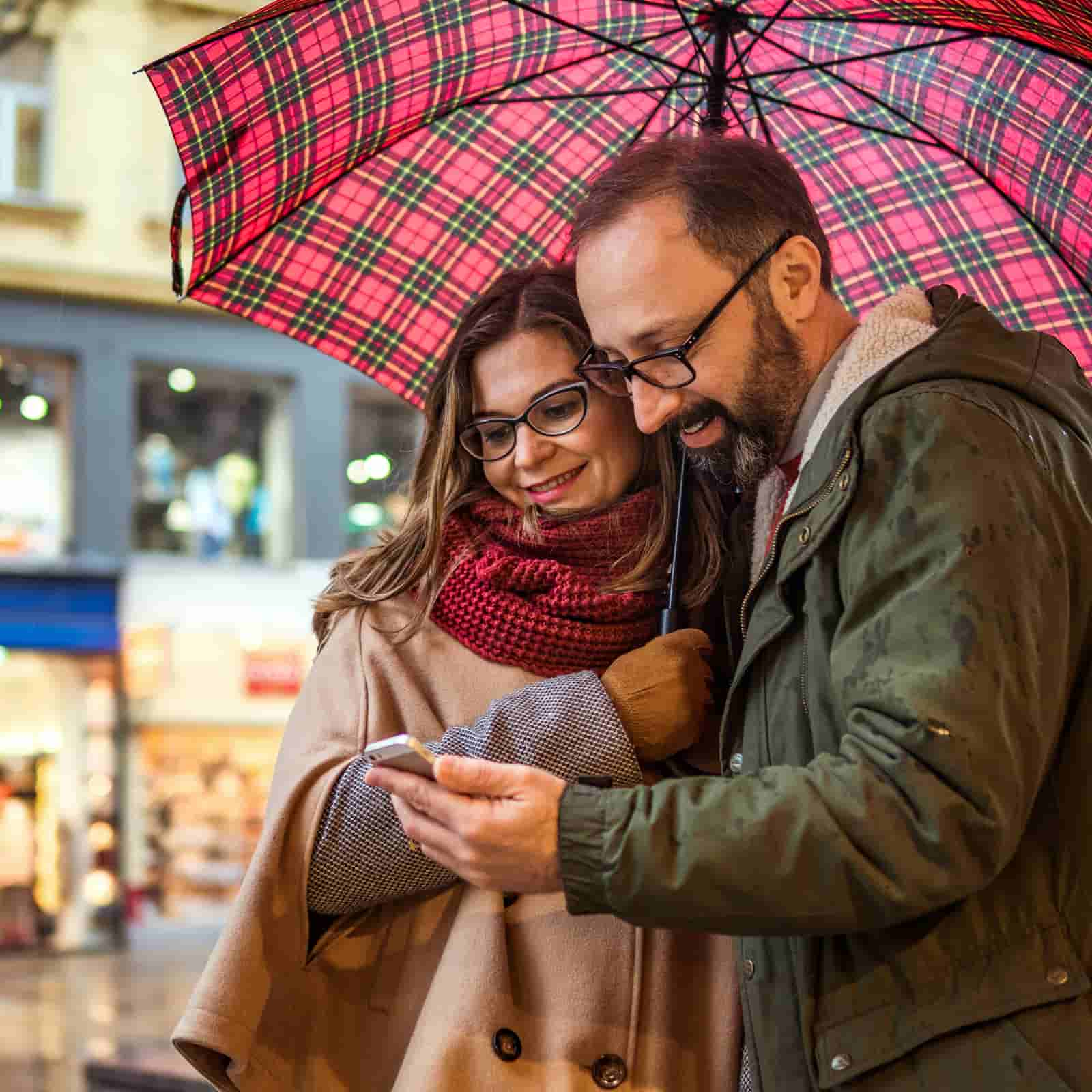 man and woman looking at a phone, underneath an umbrella