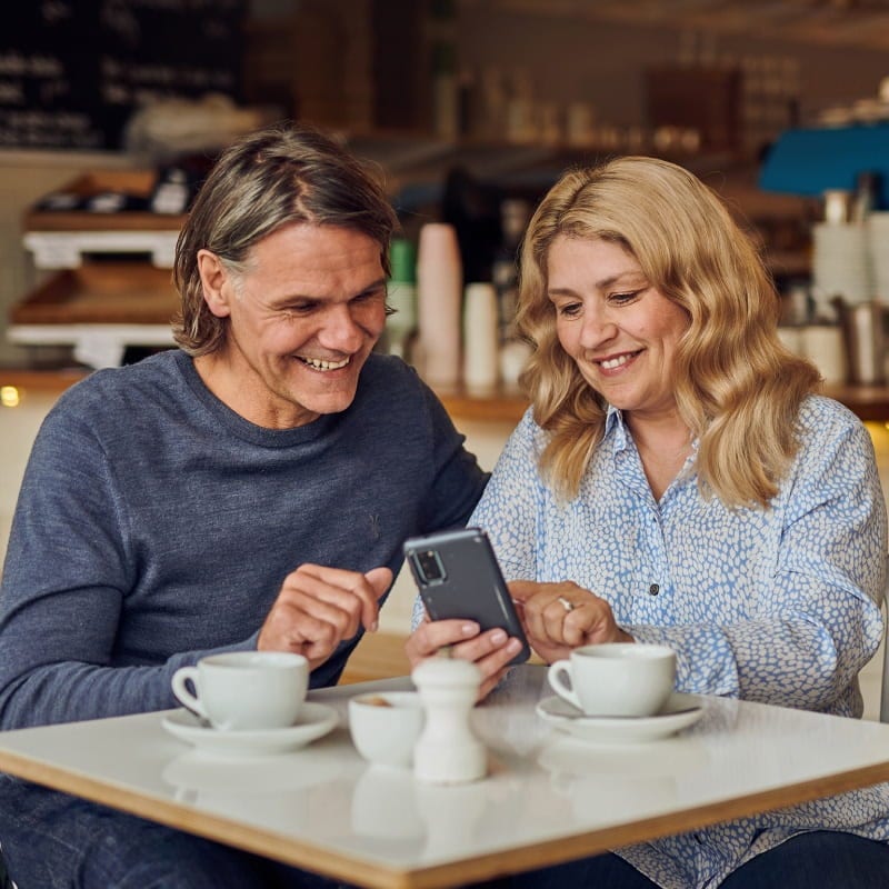 man and woman sitting down with coffee looking at phone