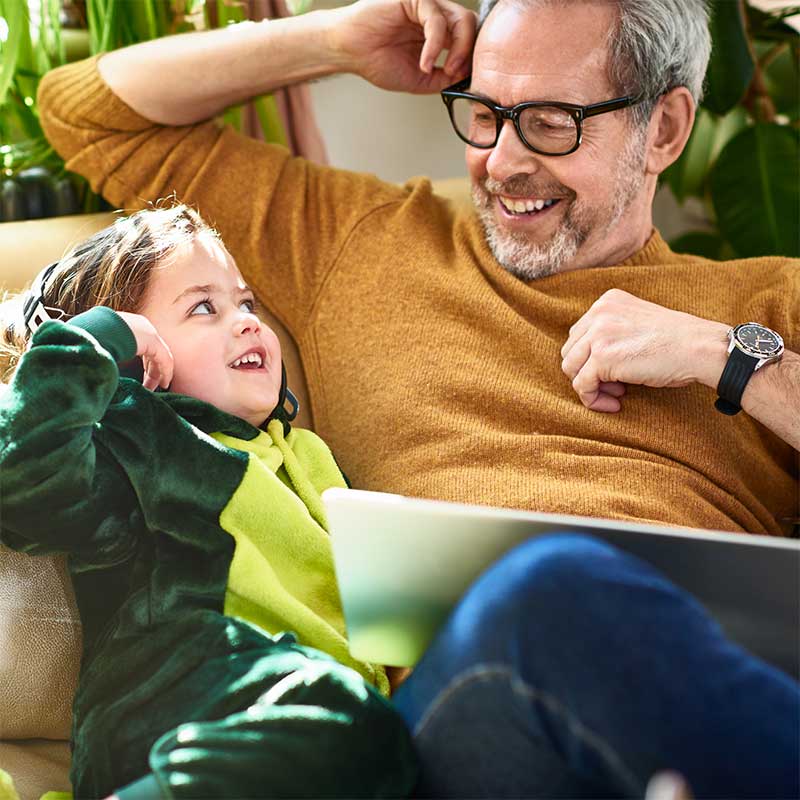 A man and a young child sat on a sofa smiling at each other