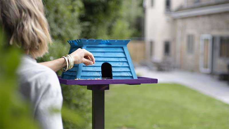 Woman putting seeds in a birdfeeder shaped like the Skipton Logo. 