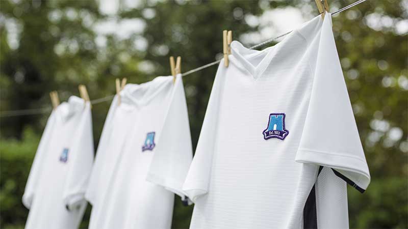 Three white shirts embroidered with the Skipton Logo. The Skipton Logo is a blue castle silhouette with the words "Est. 1853" underneath