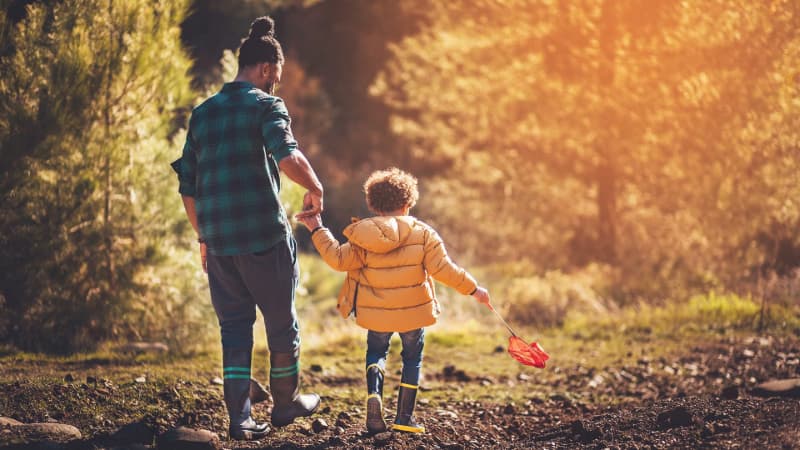 Man and young child holding hands walking in woods