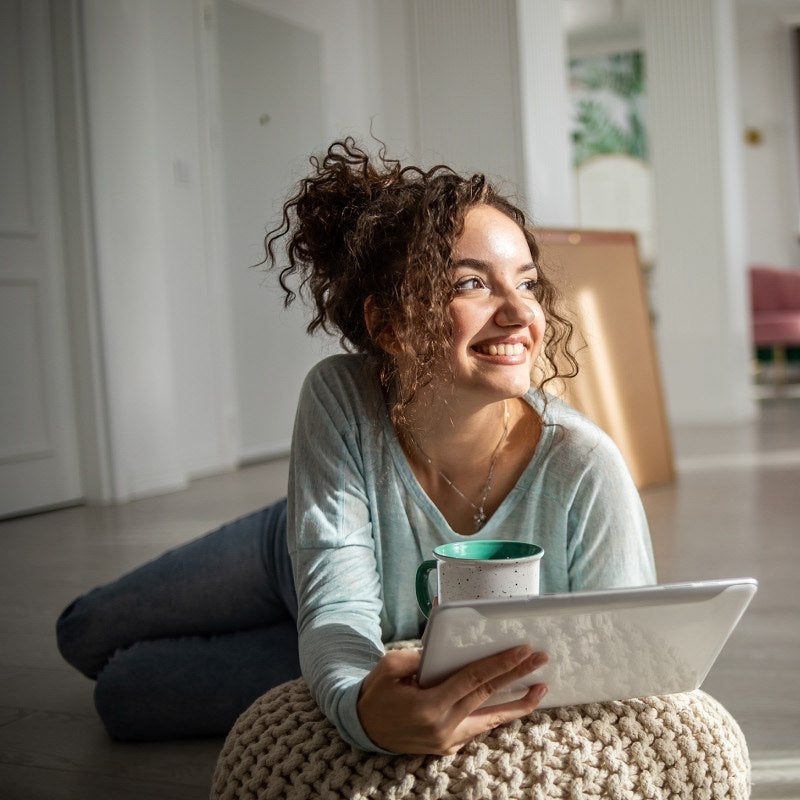 A young woman smiling and lying on the floor using a tablet