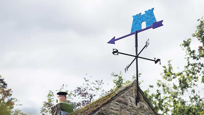 A windvane of the Skipton Building Society logo. The windvane is a blue castle with a purple arrow pointing in the wind direction